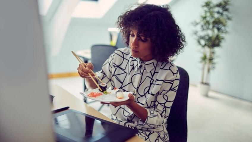 African businesswoman eating sushi at her desk in the office.