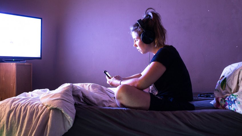 Young woman watching movie on television in bed at night.