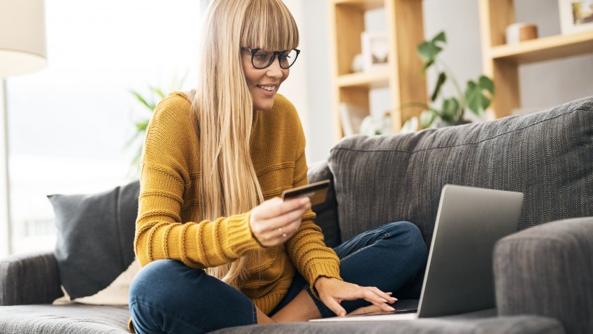 Shot of a young woman using a laptop and credit card on the sofa at home.