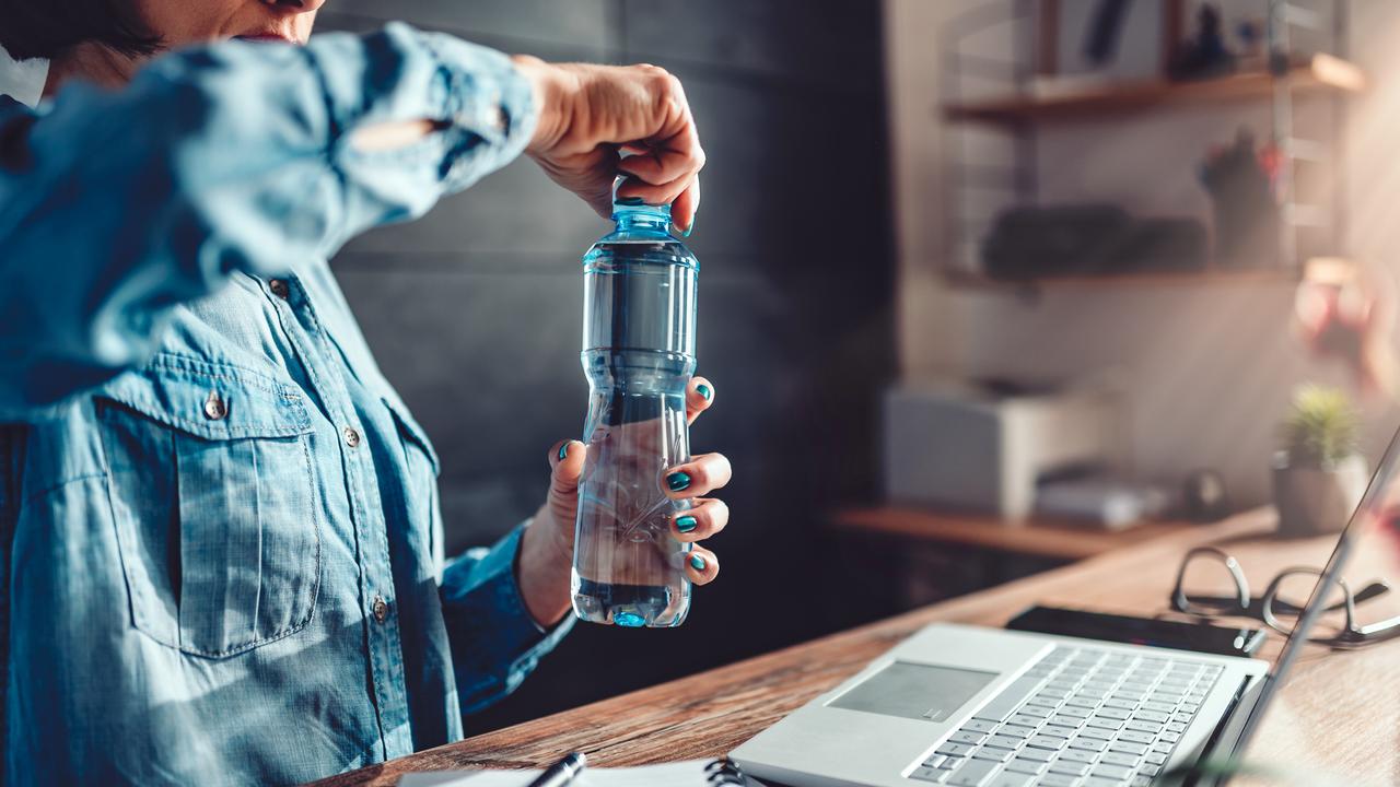Woman wearing denim shirt working in the office and opening plastic bottle of water.