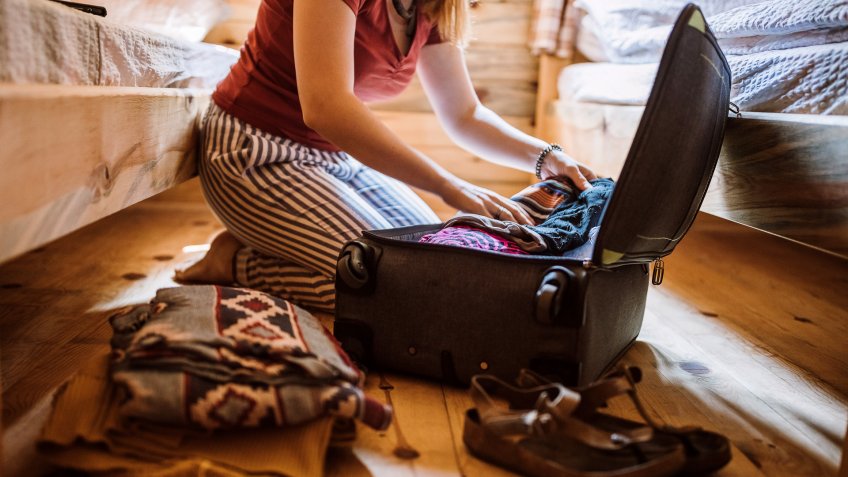 Unrecognizable woman packing luggage in log cabin, sitting on floor.