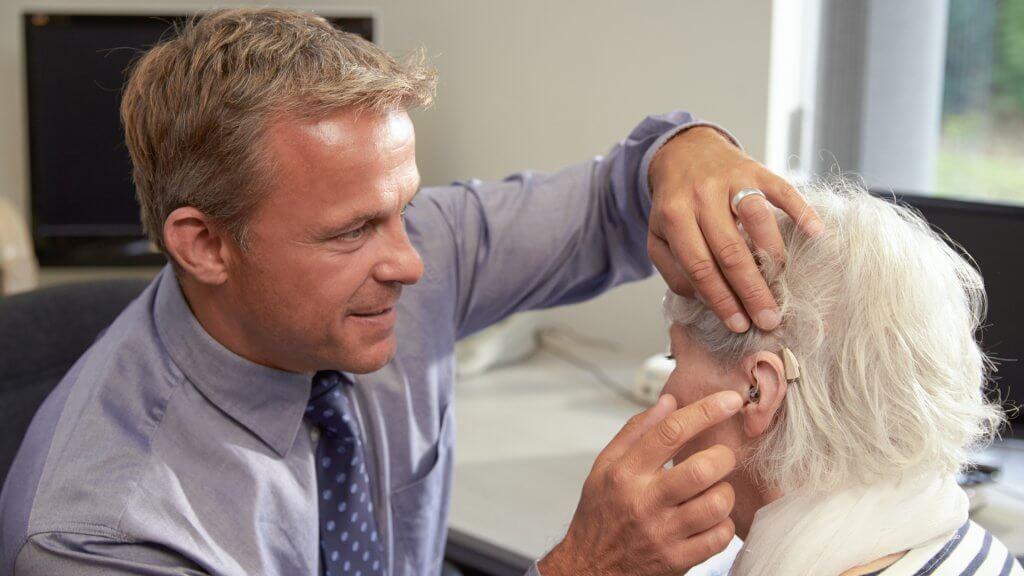 Doctor Fitting Senior Female Patient With Hearing Aid.