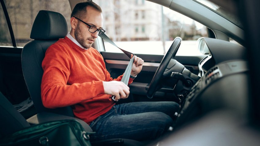 Photo of young man pulling seat belt in the car.