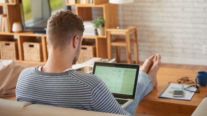 Rear view of businessman sitting on sofa at home and planning his work.