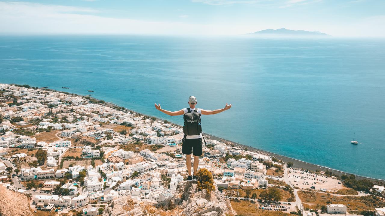 Man sitting on the rock and looking down on Kamari village with the beach in Santorini island, Greece.