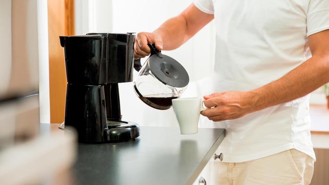 Man in the kitchen pouring a mug of hot filtered coffee from a glass pot.