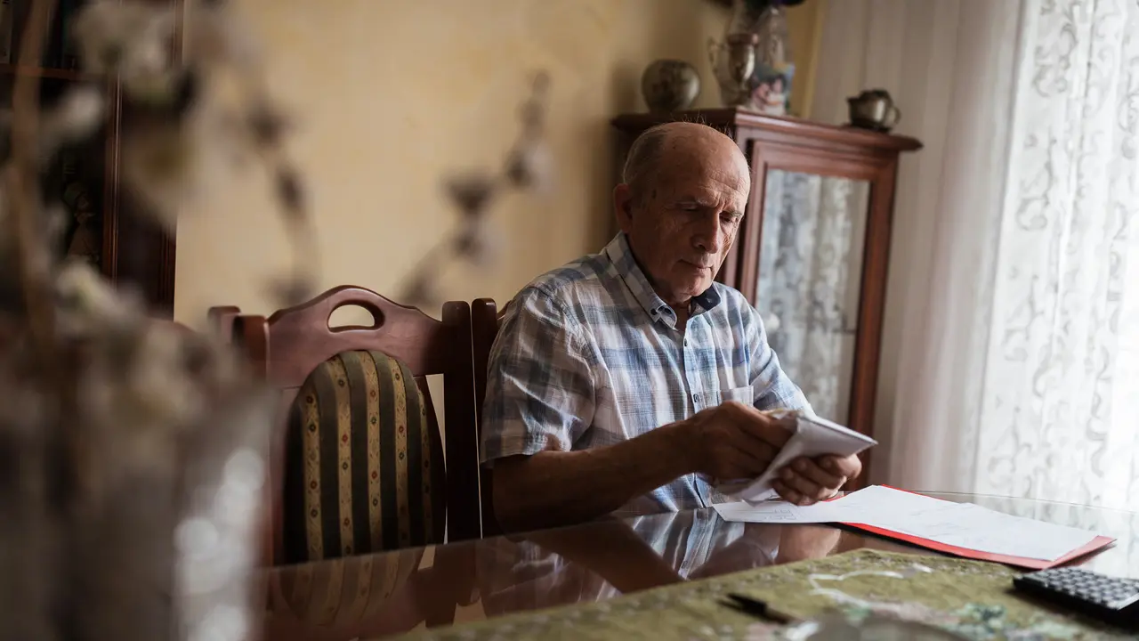 Serious old man trying to make an envelope at home.
