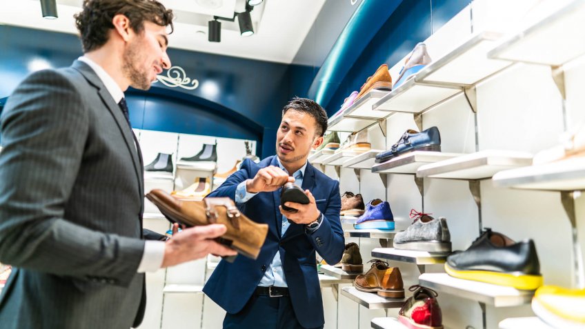 Chinese seller man showing to young handsome businessman in suit leather shoes in shopping store.