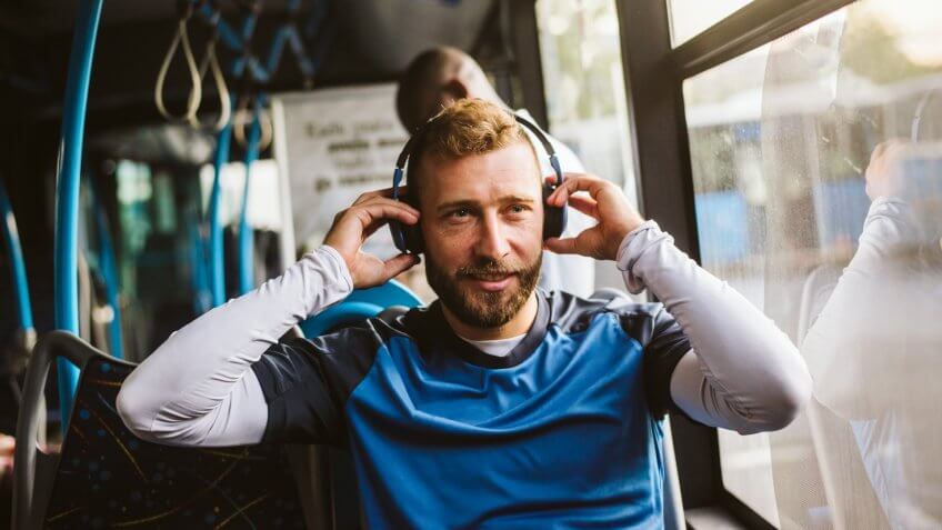 Man is sitting in a bus with headset on his head and listening to the music.