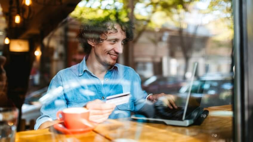 Young handsome Caucasian man using credit card for online on laptop at a cafe.