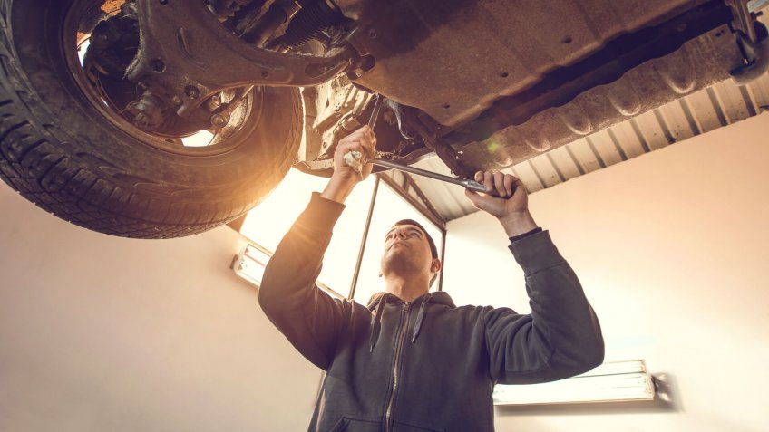 Low angle view of auto mechanic working on a chassis of a car in auto repair shop.