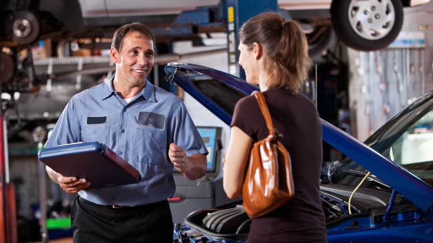 Auto mechanic with female customer discussing car repairs.