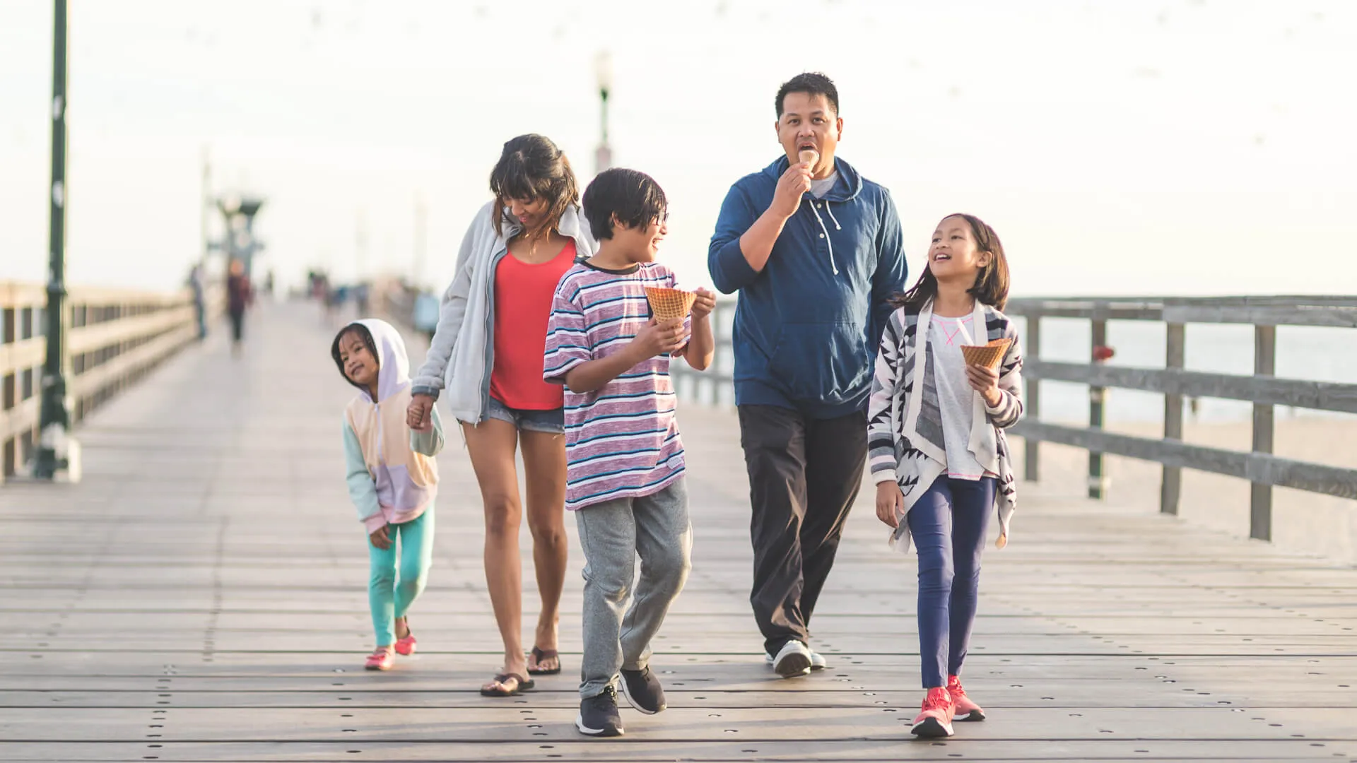 两名菲律宾父母和他们的三个孩子在加利福尼亚海滩旁的木板路上享受巨大的华夫冰淇淋甜筒。