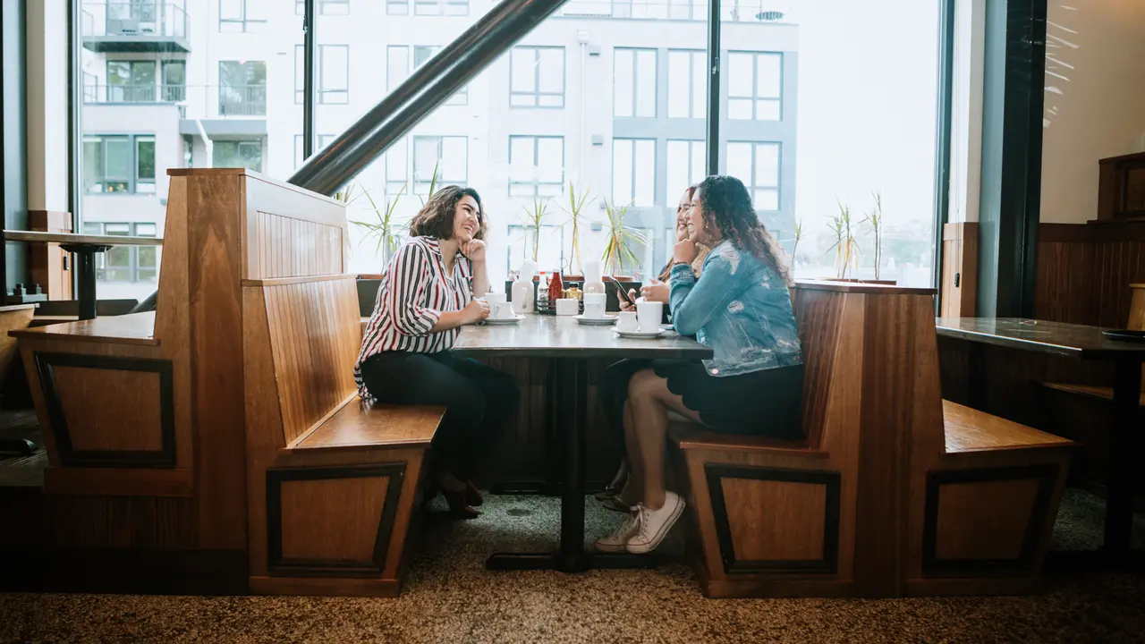 Three Hispanic women enjoy coffee at a cafe diner, having fun sharing life experiences and memories.
