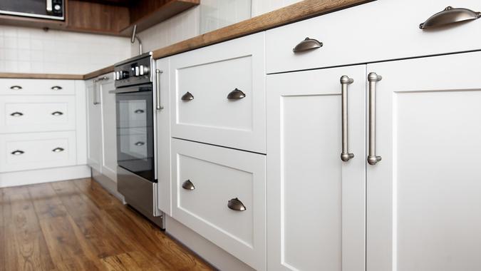 Stylish light gray handles on cabinets close-up, kitchen interior with modern furniture and stainless steel appliances.