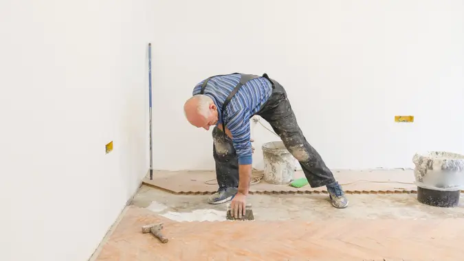 Parquet Carpenter Worker is Adding Glue on Base During Indoor Wood Flooring.