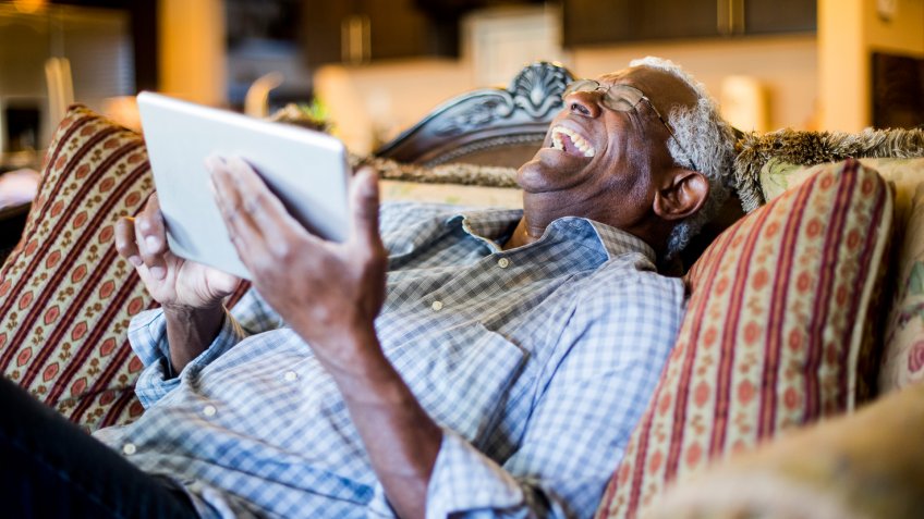 A senior black man streams content on a tablet.