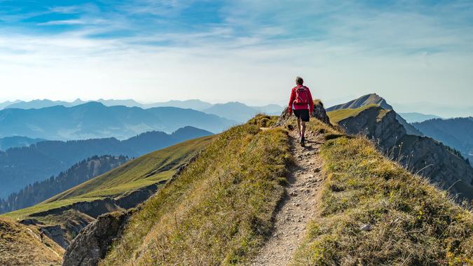 nice senior woman, hiking in fall, autumn  on the ridge of the Nagelfluh chain near Oberstaufen, Allgaeu Area, Bavaria, Germany, Hochgrats summit in the background.