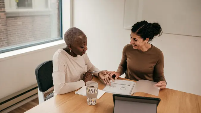 Two women seated at a conference table, reviewing financial documents in a professional setting.