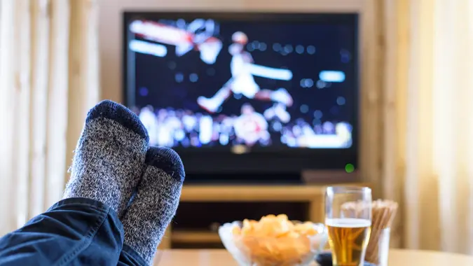 Television, watching TV (basketball game) with feet on table eating snacks and drinking beer - stock photo.