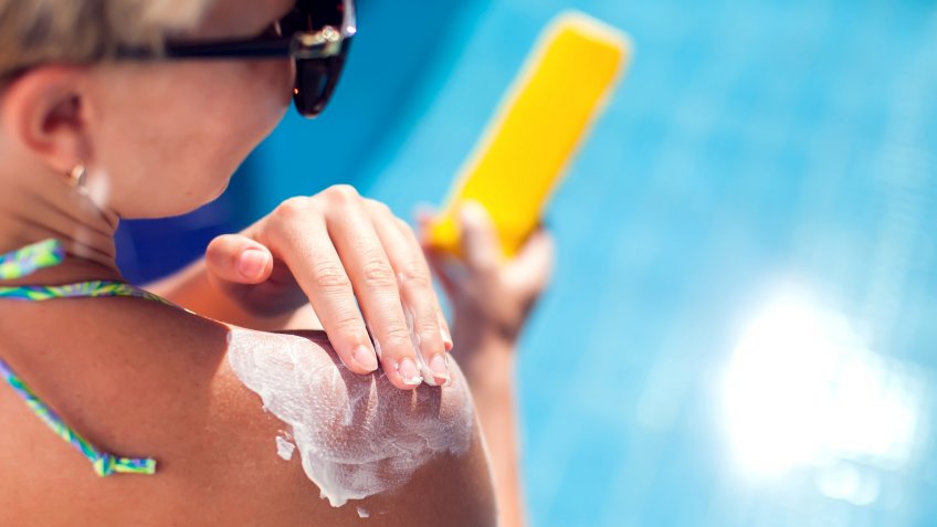 Woman applies sun protection cream on her skin sitting on the pool.