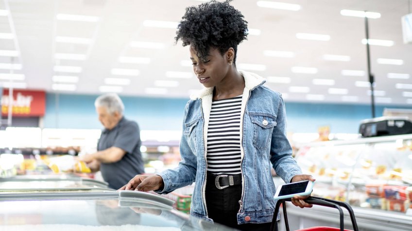 Young woman looking for products in the supermarket freezer.