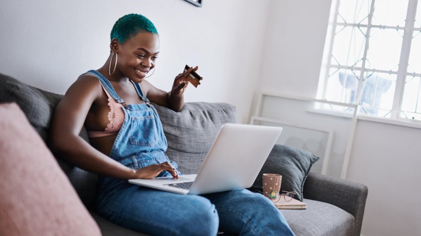 Shot of a young woman using a laptop and credit card at home.