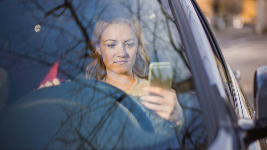 Young serious woman driving car and reading text message on cell phone.