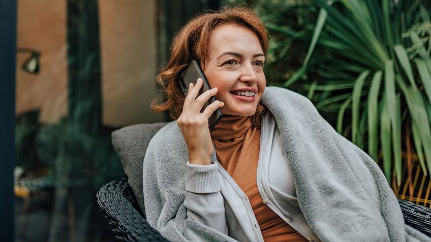 Successful woman talking on smart phone on the patio of modern house, portrait, copy space.