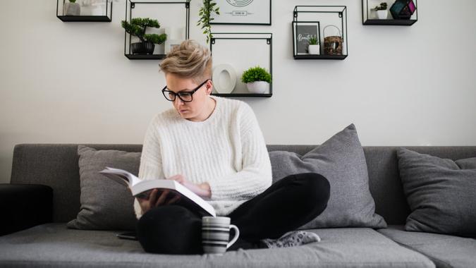 Happy woman reading book on couch at home.