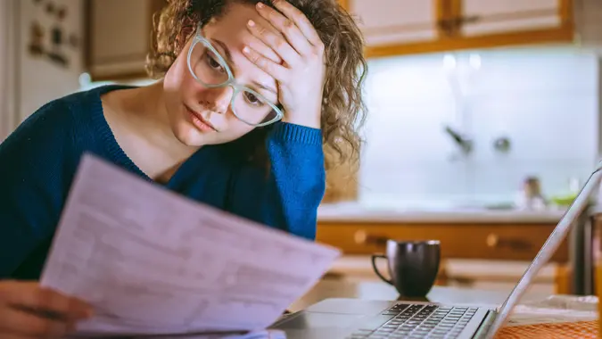 Young female reading documents, using laptop in the kitchen at home.