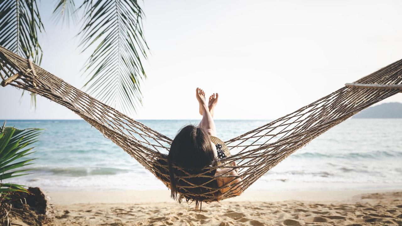 Summer vacations concept, Happy woman with white bikini, hat and shorts Jeans relaxing in hammock on tropical beach at sunset, Koh mak, Thailand.