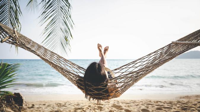 Summer vacations concept, Happy woman with white bikini, hat and shorts Jeans relaxing in hammock on tropical beach at sunset, Koh mak, Thailand.