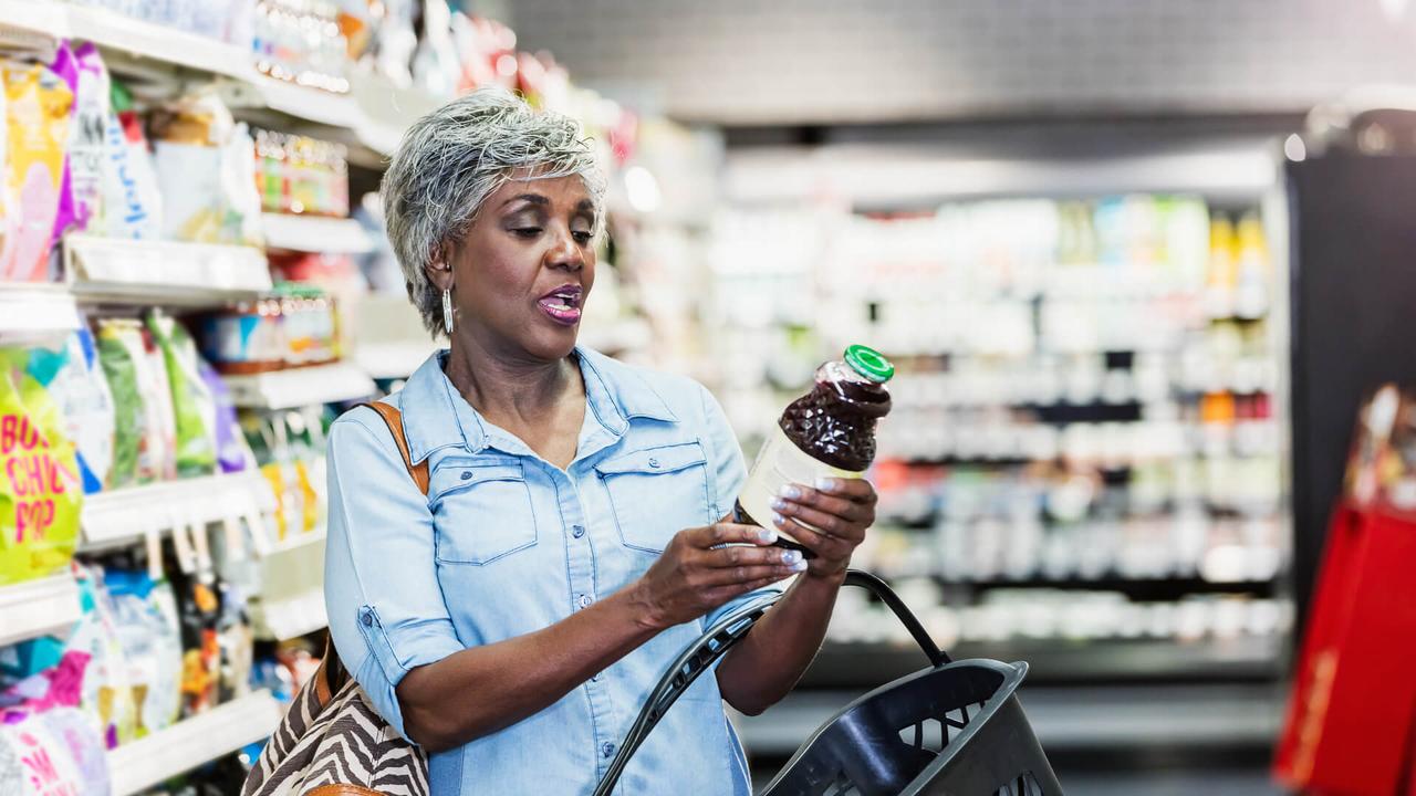 A senior African-American woman in her 60s shopping in a grocery store, carrying a shopping basket.