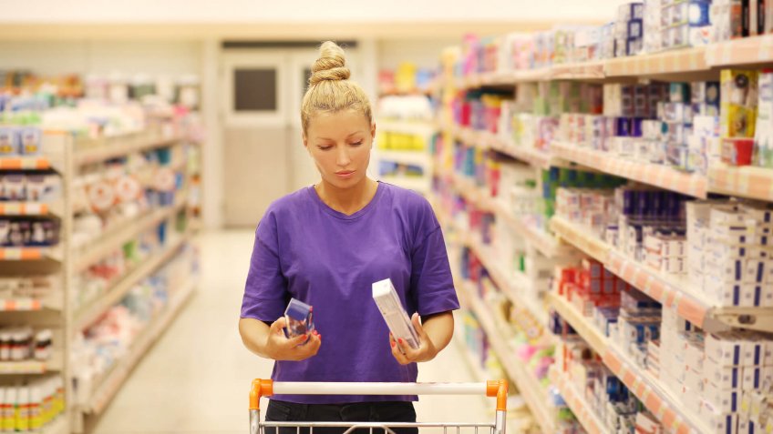 Woman shopping in supermarket reading product information.