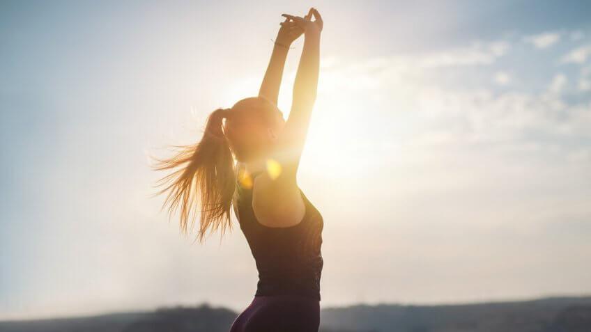Young women in sports clothing feeling freedom in nature, doing gymnastics on sunset with lens flare.