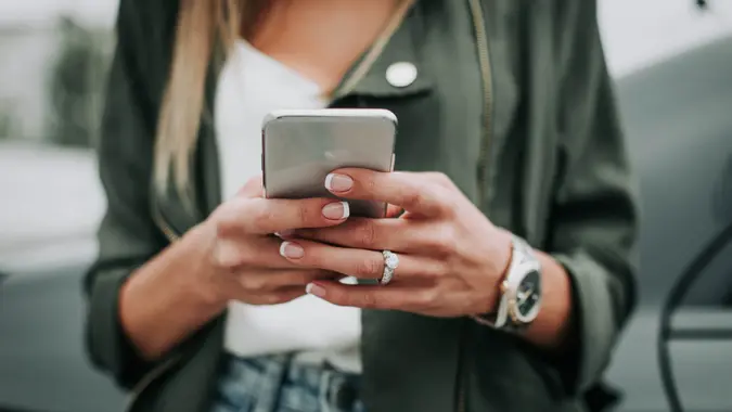 Cierre el brazo femenino enviando un mensaje por teléfono mientras usa relojes y anillos contemporáneos.