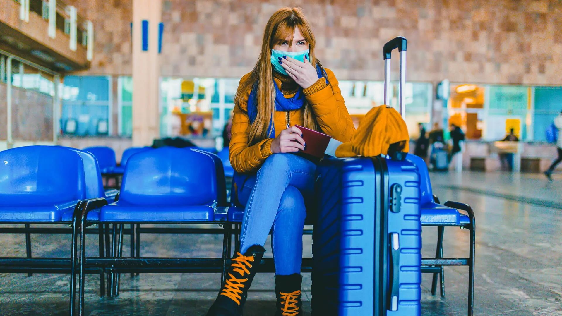 Young woman wearing a protective face mask and waiting for a train at the airport station.