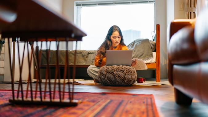 A young woman is using a laptop comfortably in the living room at home.