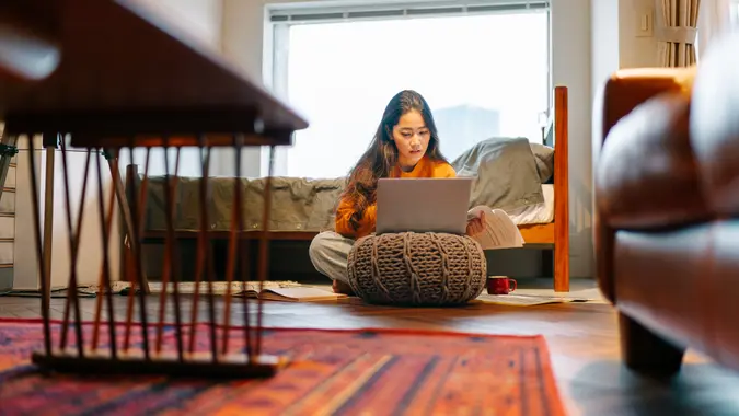 A young woman is using a laptop comfortably in the living room at home.