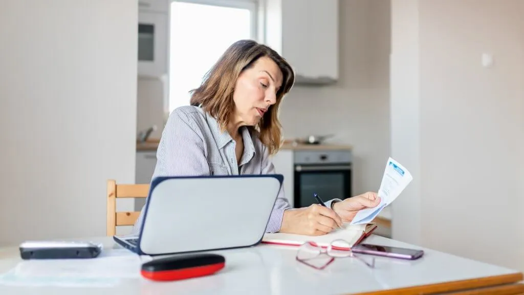 Busy Senior Woman Writing Notes While Working From Home Office Space.