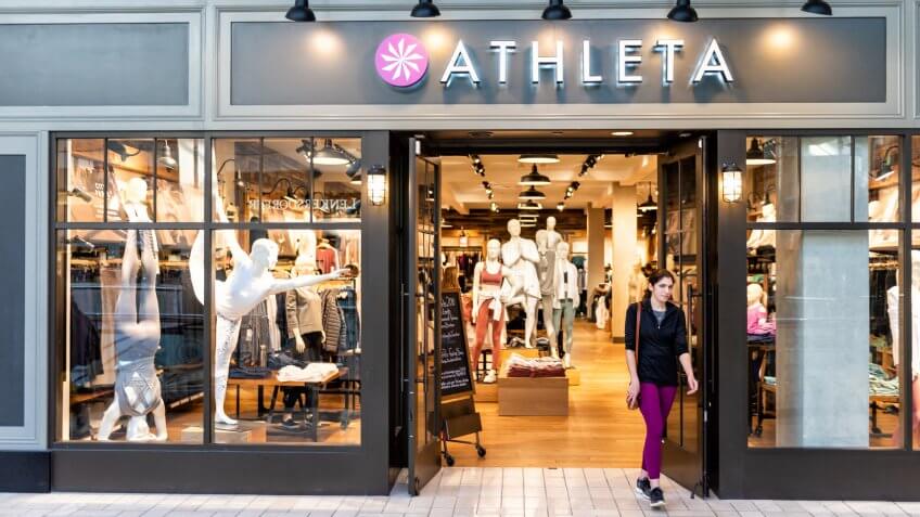 Tysons Corner, USA - January 26, 2018: Athleta store, shop, facade, storefront, door entrance with people, young woman walking in shopping mall in Virginia.