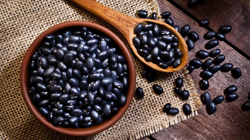 Top view of a brown bowl filled with black beans shot on rustic wood table.