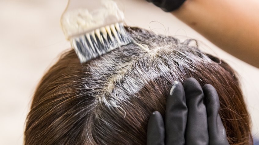 Closeup of hair dresser applying chemical color dye onto hair of customer in salon.