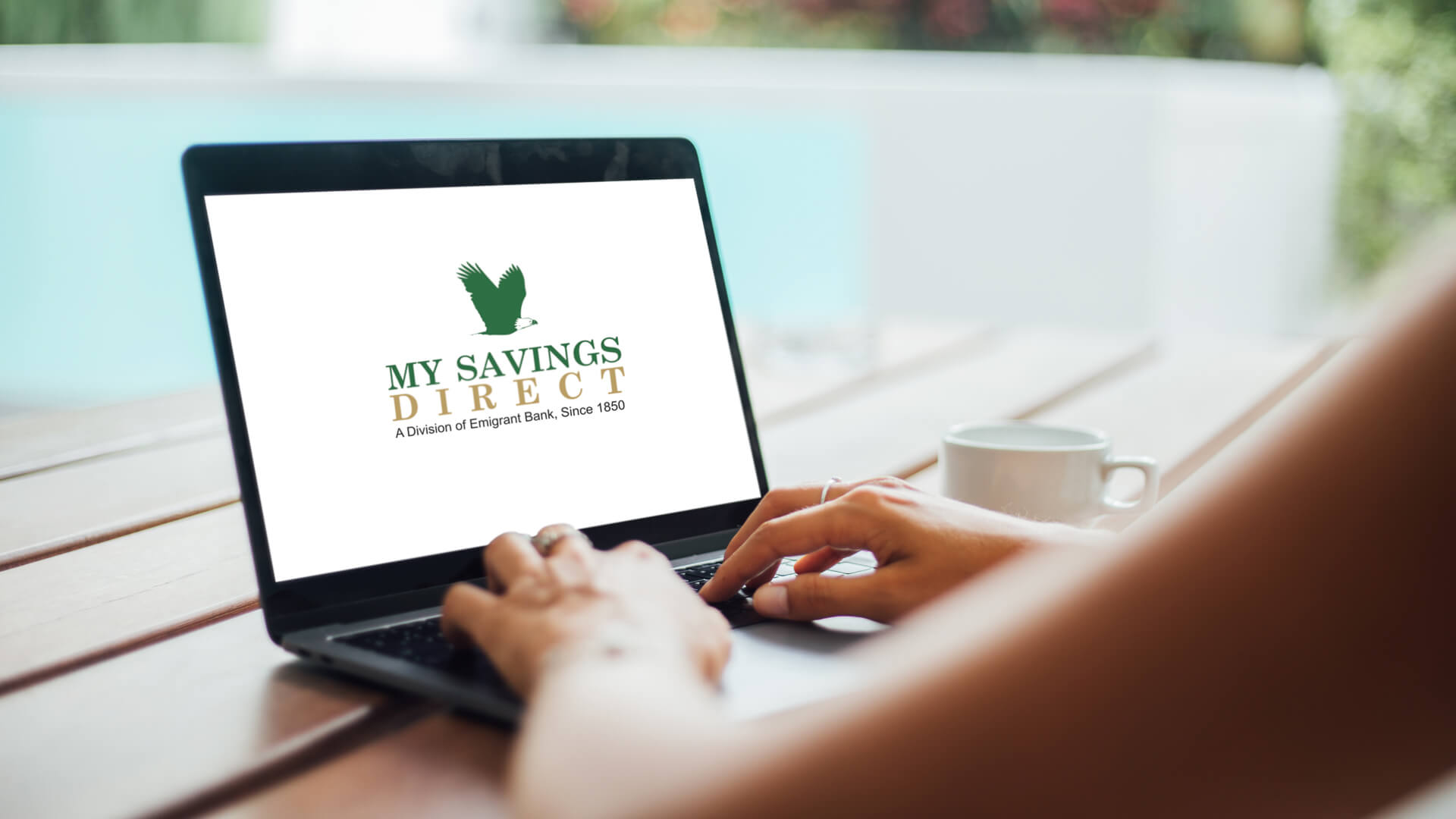Woman working with laptop with blank screen sitting at swimming pool.