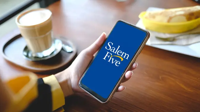 Close-up of a woman holding a smartphone, with the Salem Five logo clearly displayed on the screen in focus.