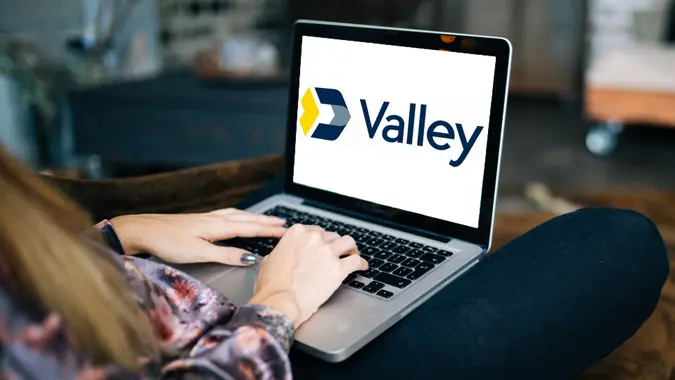 Shot of a young woman sitting on her couch using laptop with the Valley Bank logo on the screen.