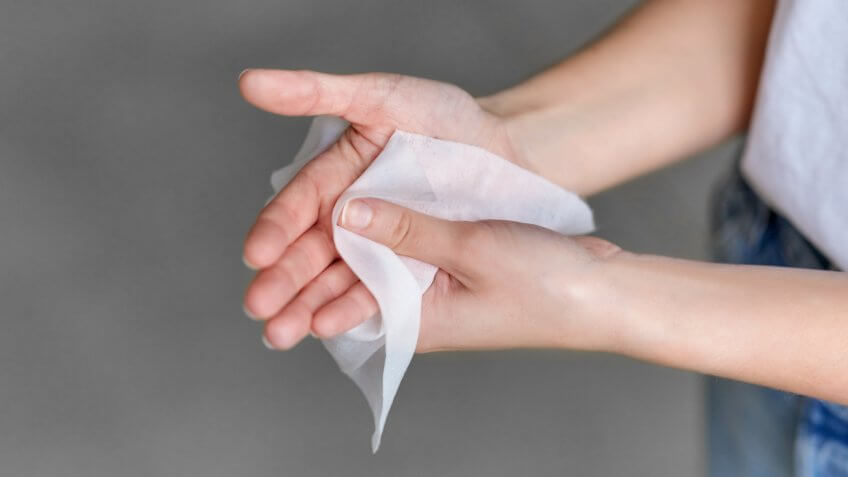 hygiene, health care and disinfection concept - close up of woman cleaning hands with antiseptic wet wipe.
