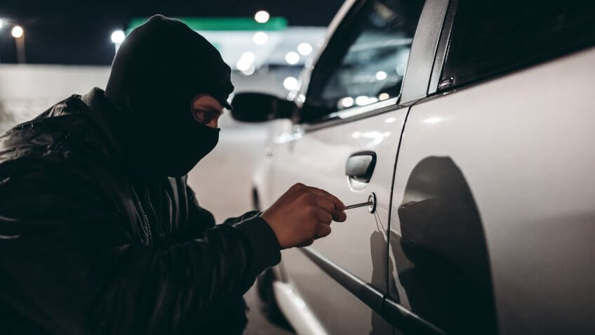 Caucasian man with ski mask stealing a car at night.