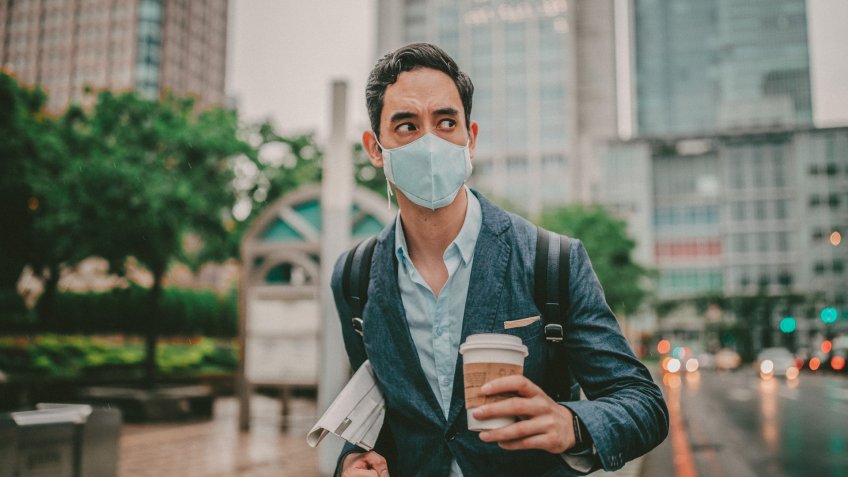 Businessman wearing surgical mask to protect from flu/air pollution in city.